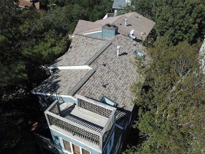 Blue house with a deck and gray roof surrounded by trees.