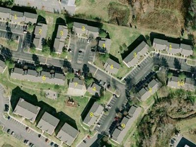 Aerial view of apartment complex with numbered buildings, parking lots, and green spaces.