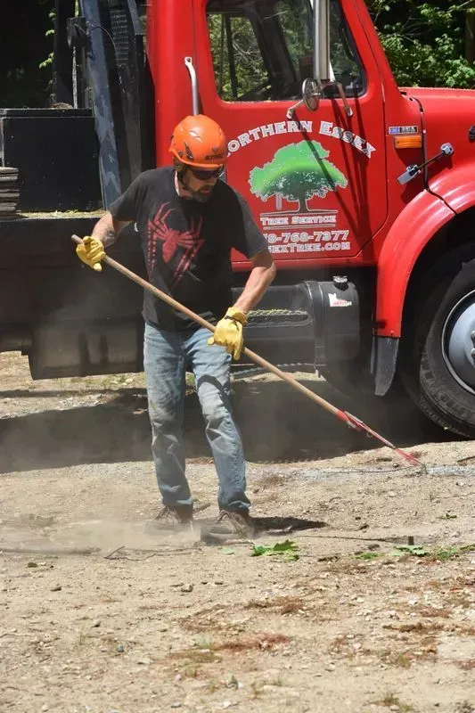 Man in orange hard hat rakes debris on a gravel road next to a red truck with 