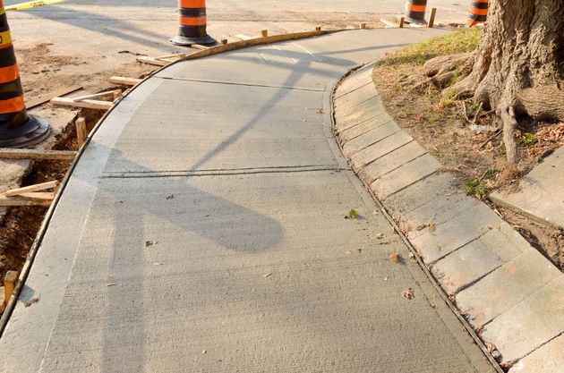 Curved sidewalk under construction beside a tree, with orange traffic cones and fresh concrete edges