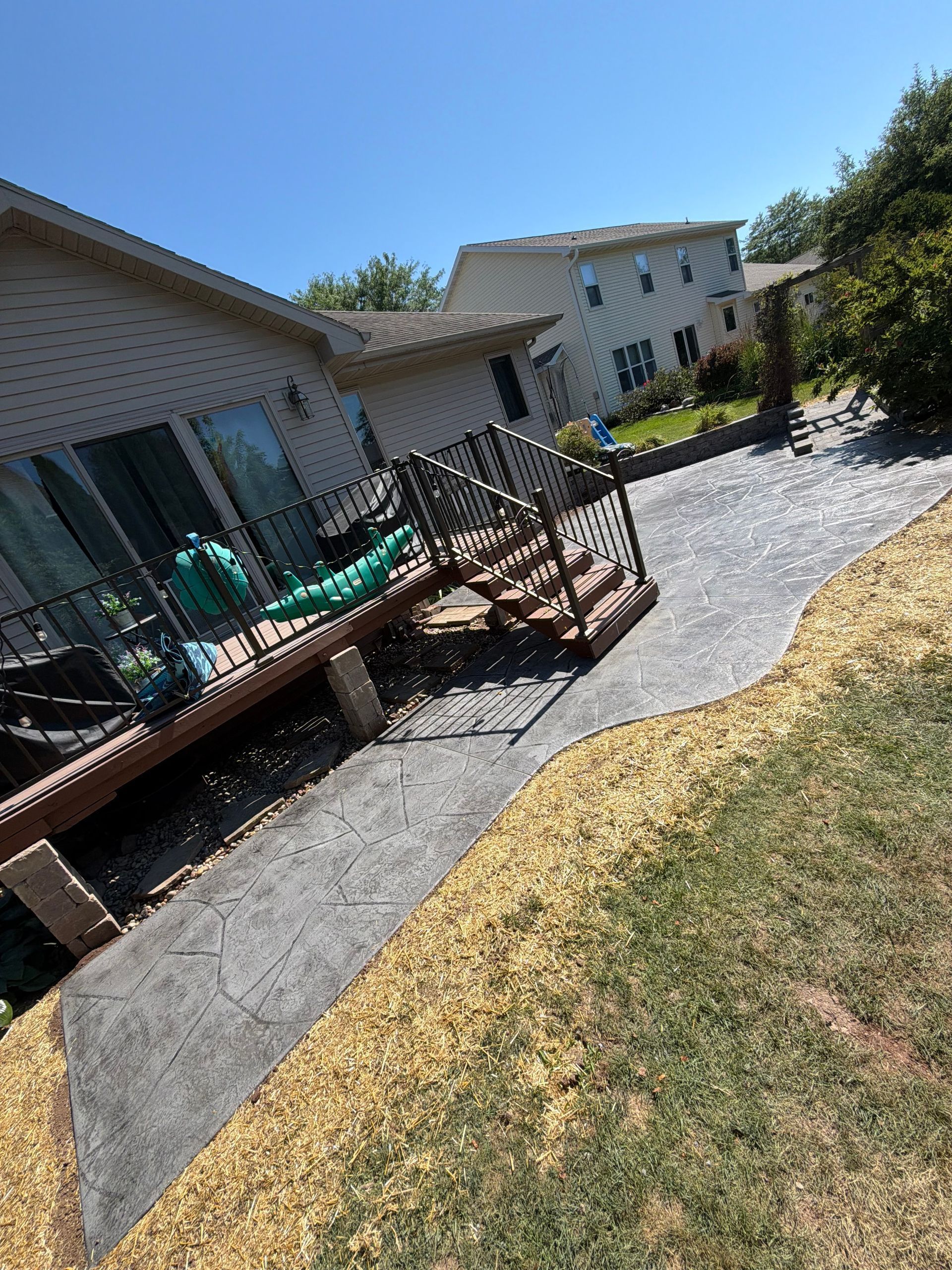 Backyard deck with black railing, gravel path, and beige house under a sunny blue sky