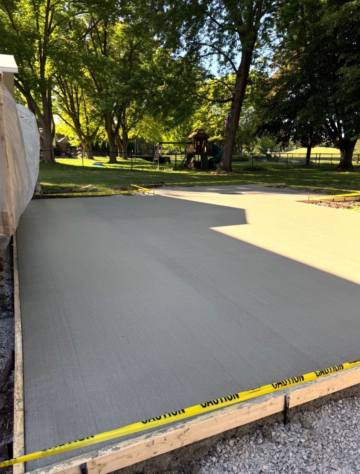 Freshly poured concrete patio slab bordered by wood formwork in a sunny park with trees.