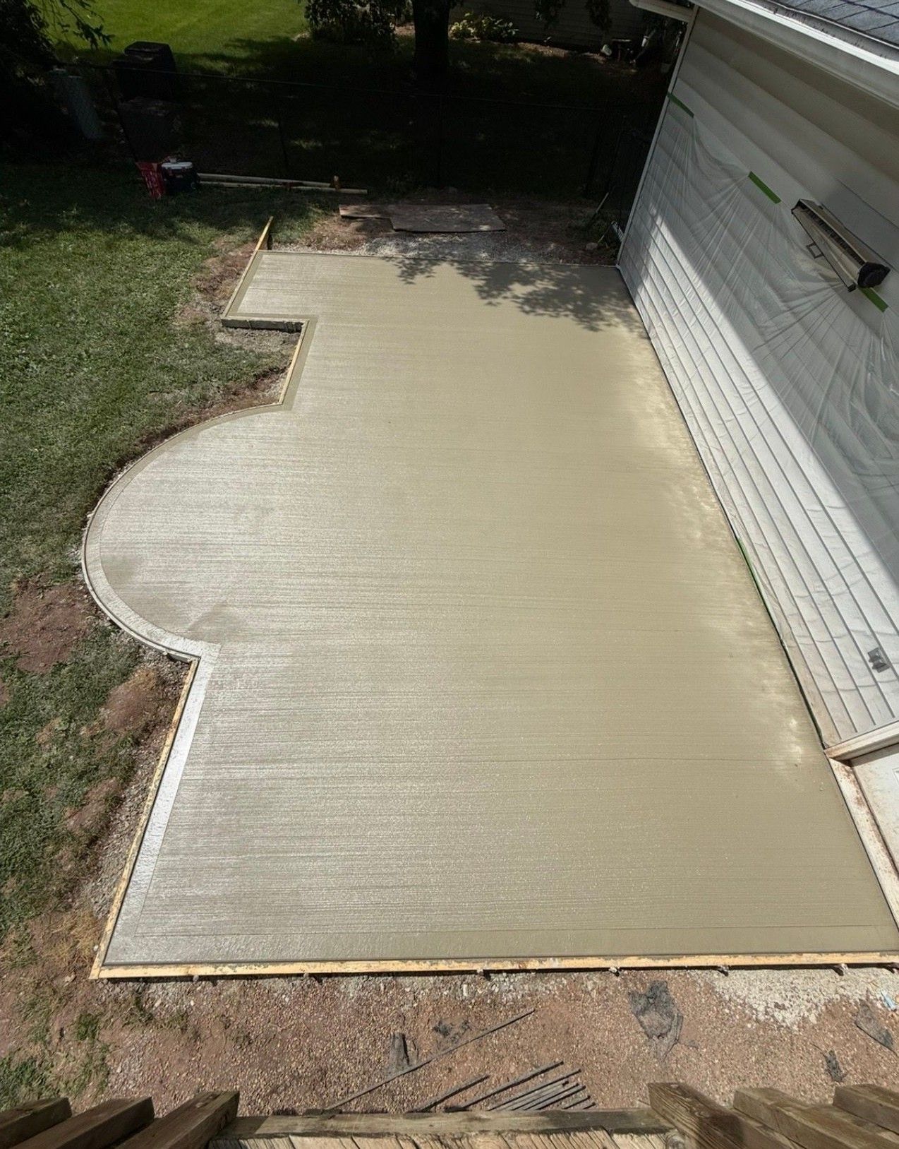 Freshly poured concrete patio beside a white house in a backyard