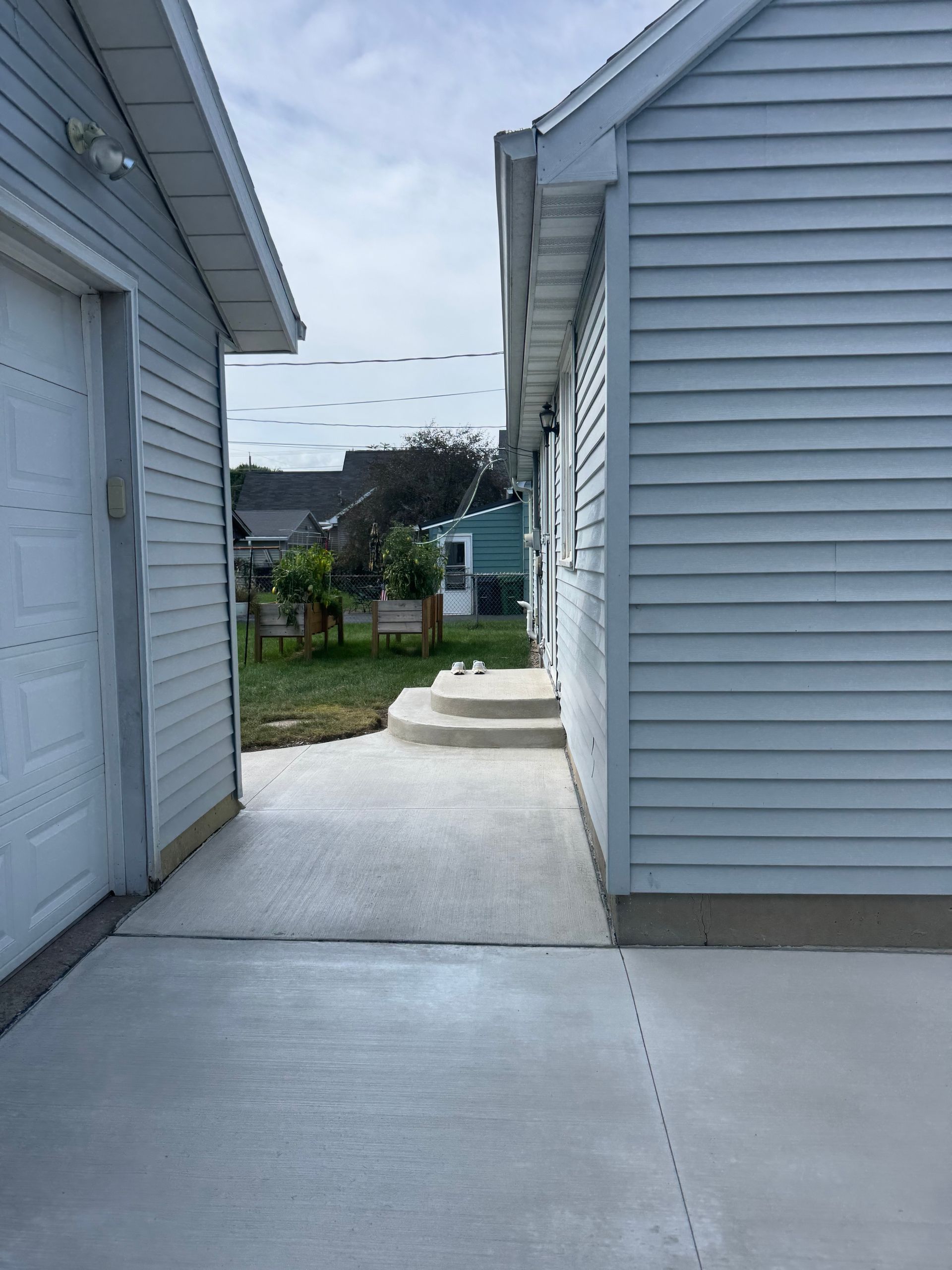 Narrow concrete walkway between two white houses leading to a backyard