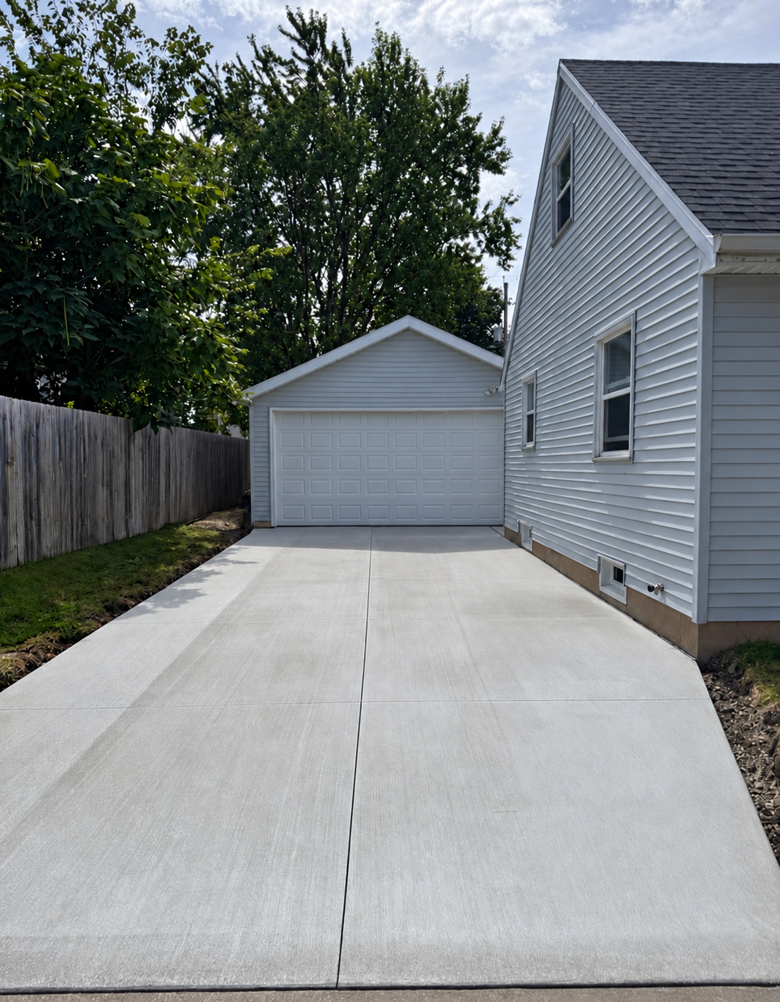 Concrete driveway leading to a white detached garage beside a house and wooden fence.