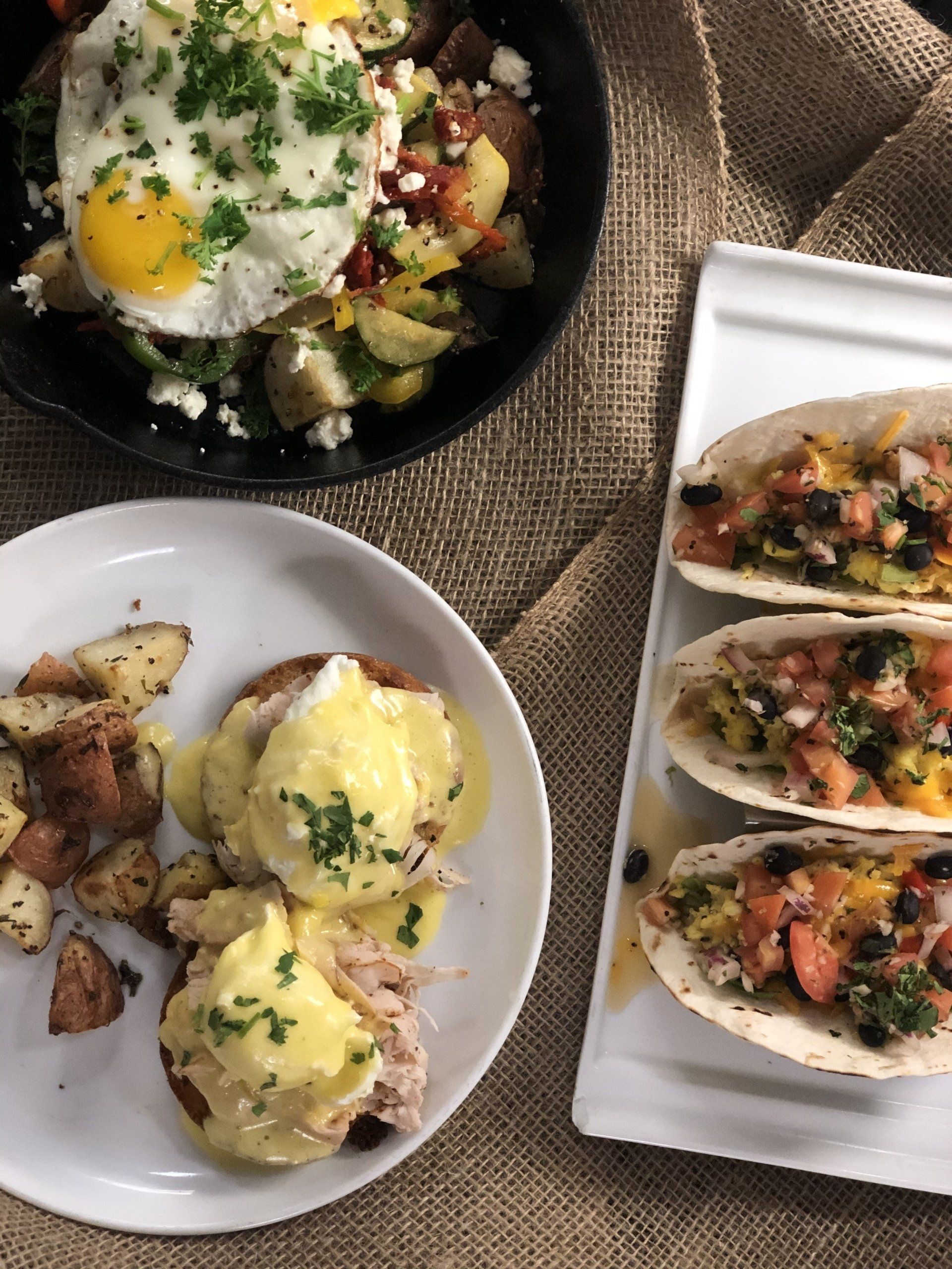 A table topped with plates of food including tacos and eggs benedict