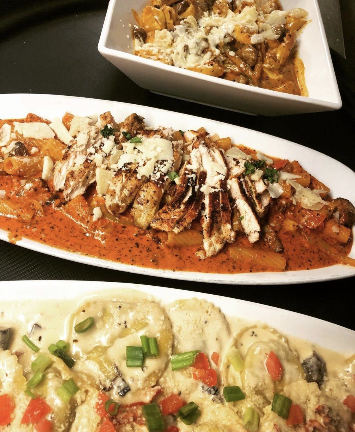 Three plates of food on a table including ravioli and chicken