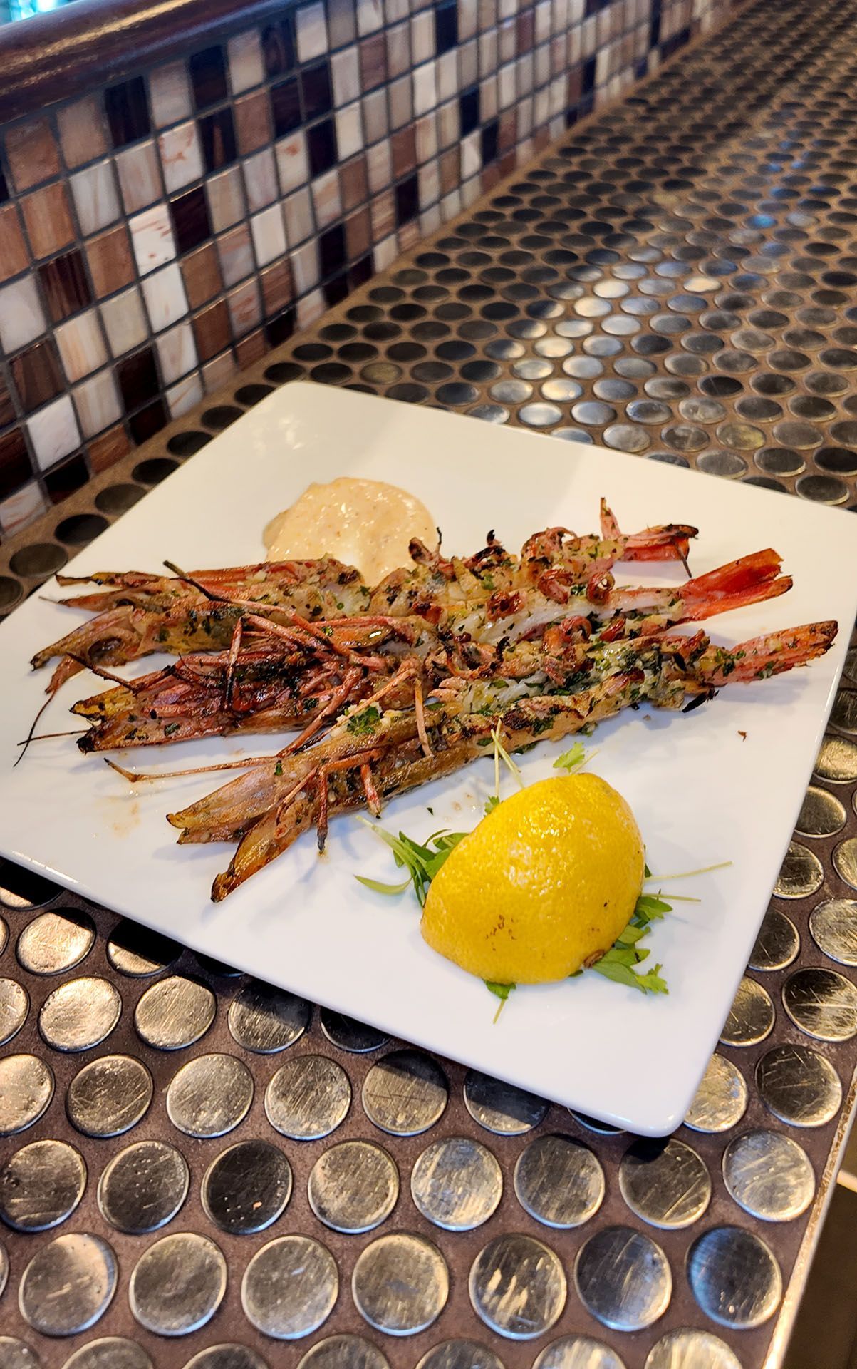 Grilled shrimp on a white plate with lemon and sauce