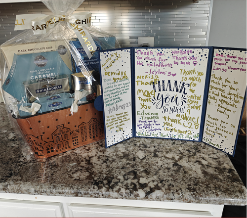 Gift basket and thank you card on a countertop. Basket contains food items; card has handwritten notes.