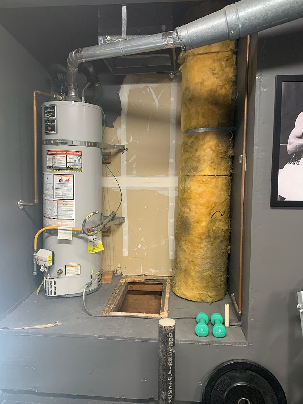 A water heater in a basement alcove, with exposed insulation and ventilation.