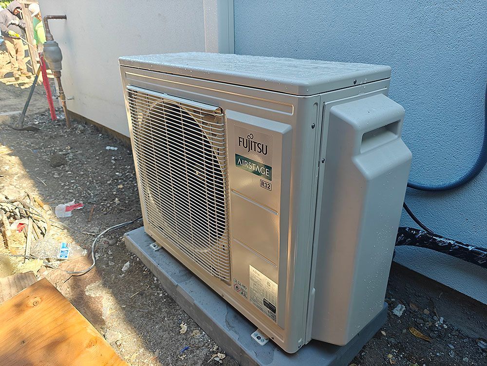 Fujitsu outdoor air conditioning unit on a concrete pad near a building's exterior wall.