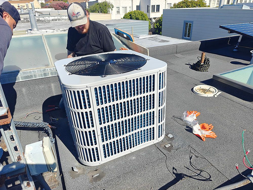 Two people working on an air conditioning unit on a rooftop.
