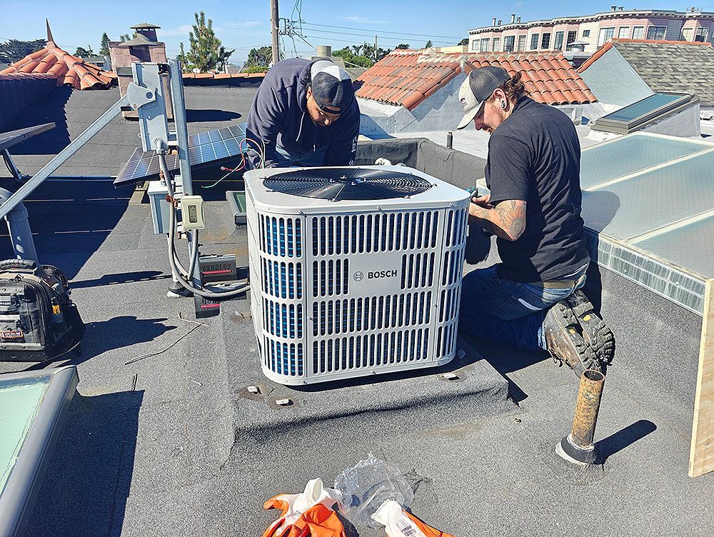 Two workers installing an air conditioning unit on a rooftop. Bright, sunny day.