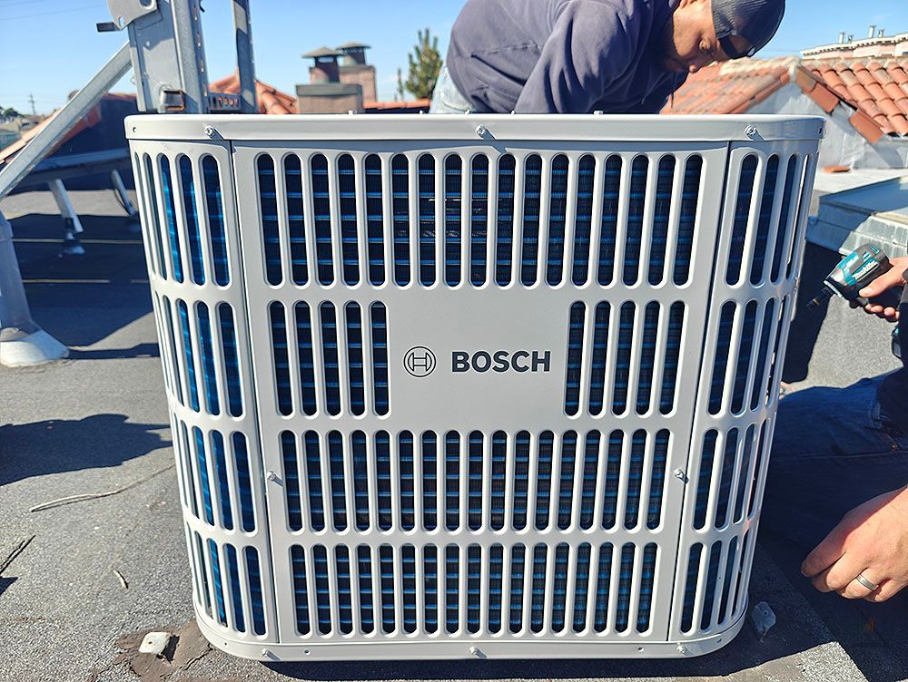 Bosch air conditioning unit on a rooftop, being installed by two people. White cage design.