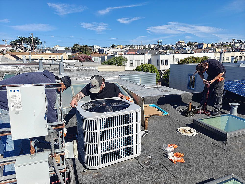 Three workers on a rooftop installing HVAC equipment on a sunny day.