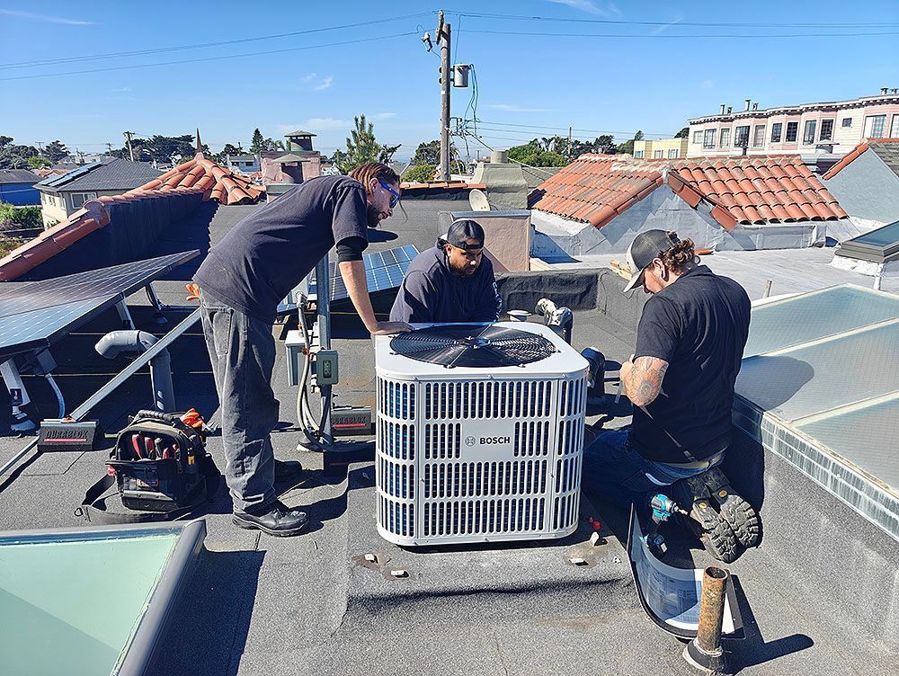 Three workers installing an HVAC unit on a rooftop on a sunny day.