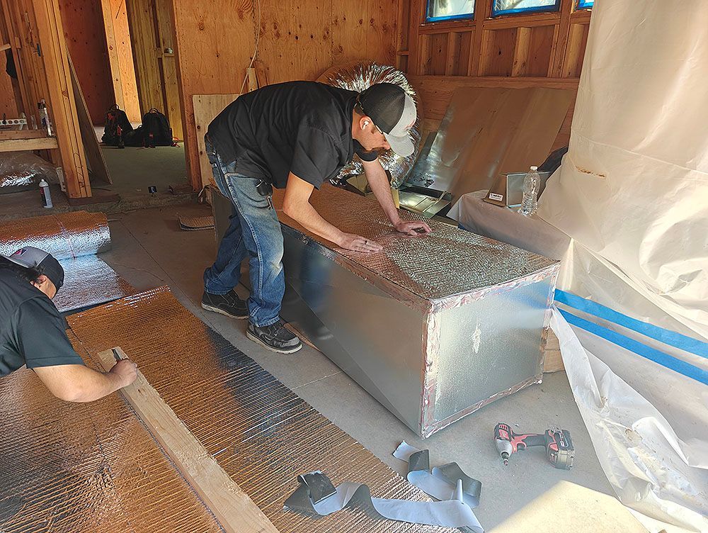 Two people insulating an HVAC unit inside a building under construction.
