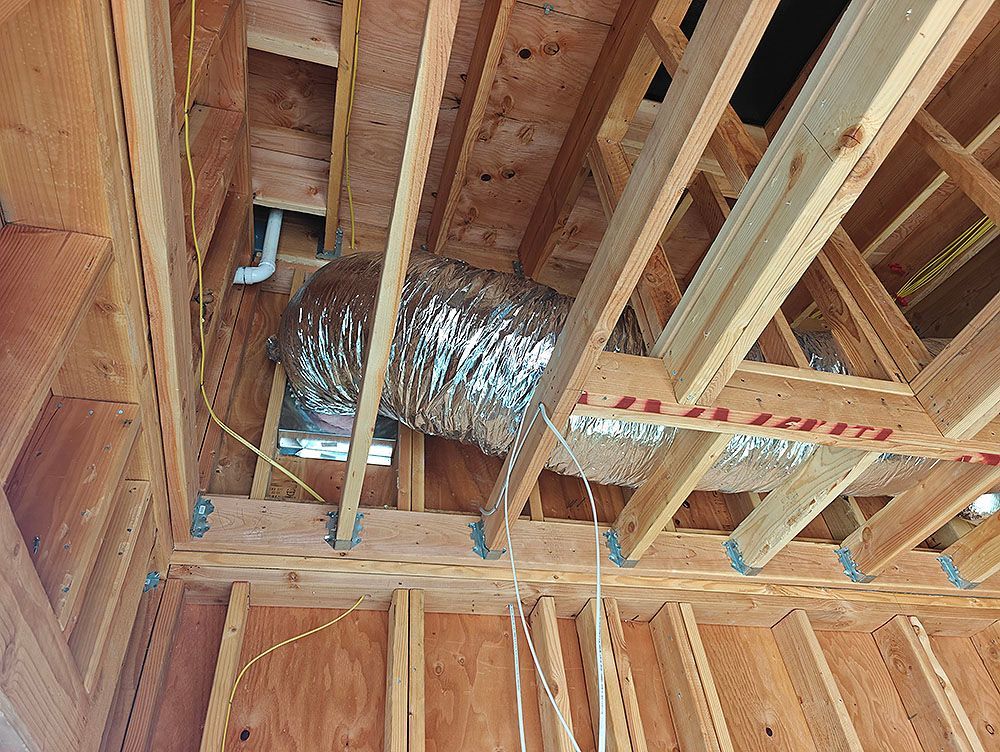 Unfinished attic framing with ductwork and wiring, seen from below.