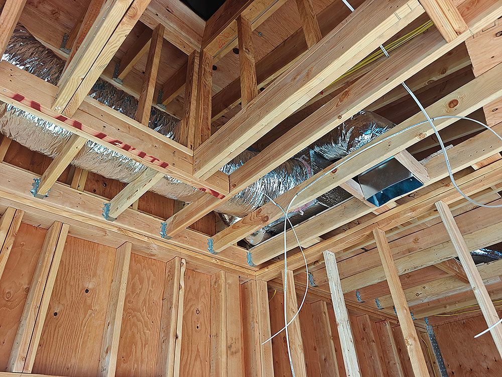 Interior view of a building under construction, showing wooden framing, ductwork, and wiring in a corner.