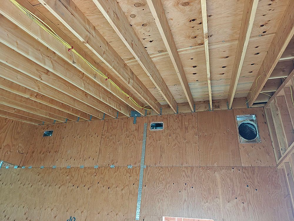 Interior view of unfinished construction. Wooden ceiling joists and plywood walls. Vent and electrical work visible.