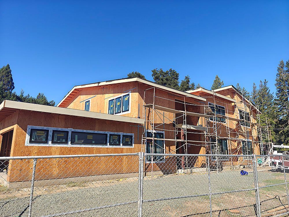 Building under construction with wood framing, windows, and scaffolding, behind a chain-link fence.