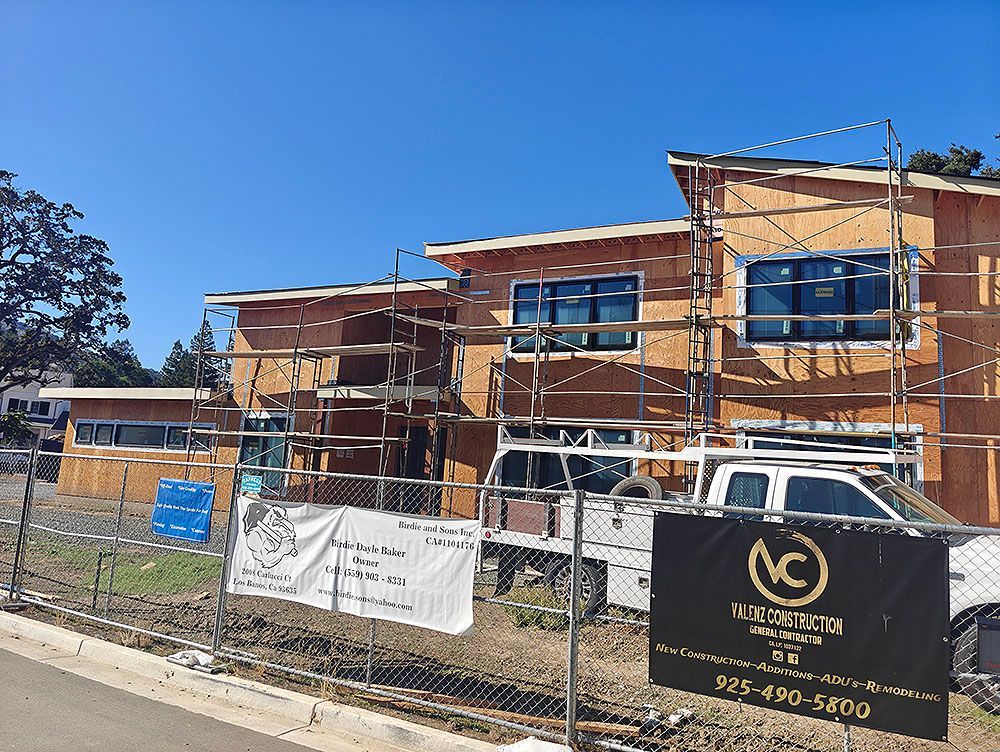 Construction of a two-story building with scaffolding. A white truck and signage are in front of the fenced area.
