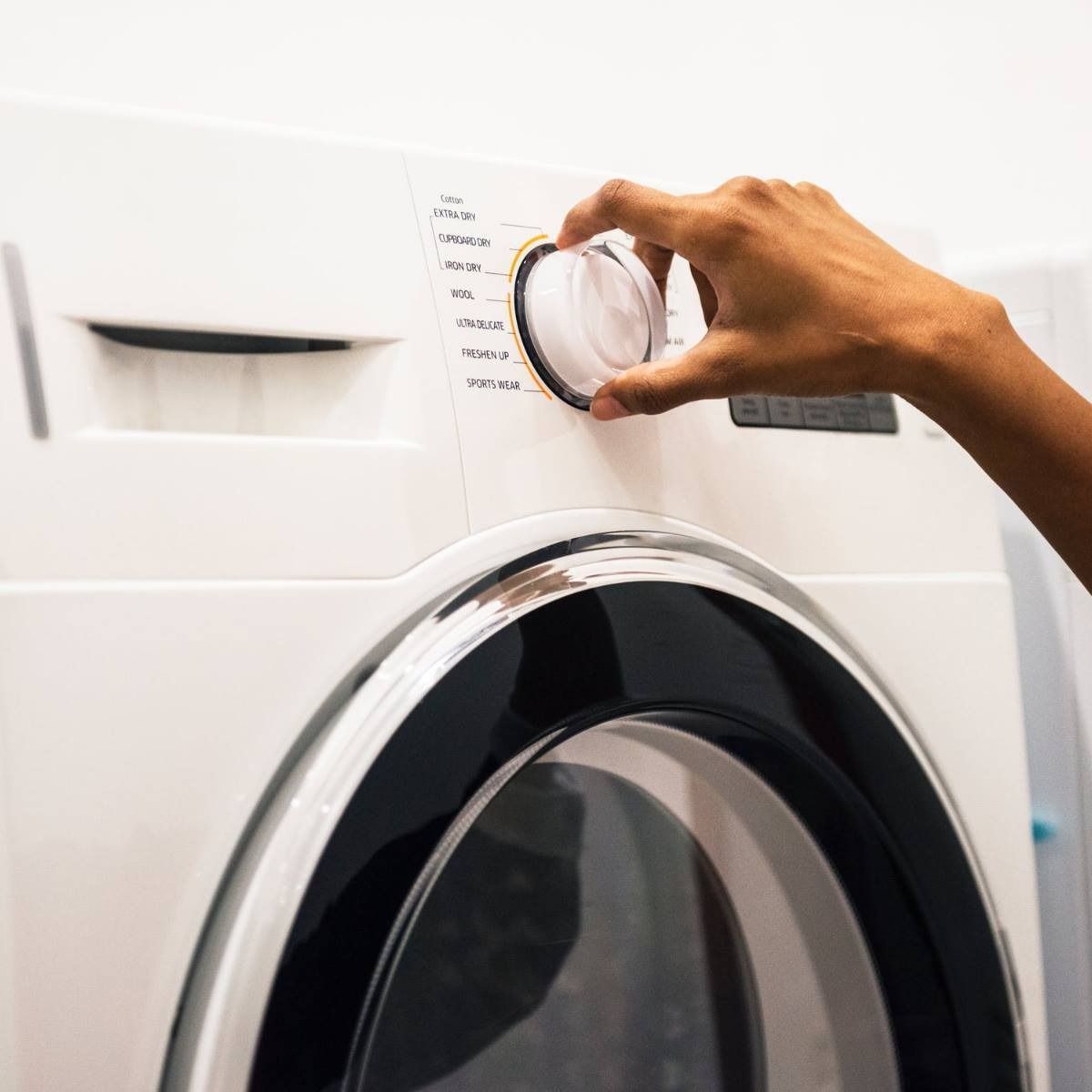 Hand turning a dial on a white washing machine to select a wash cycle.