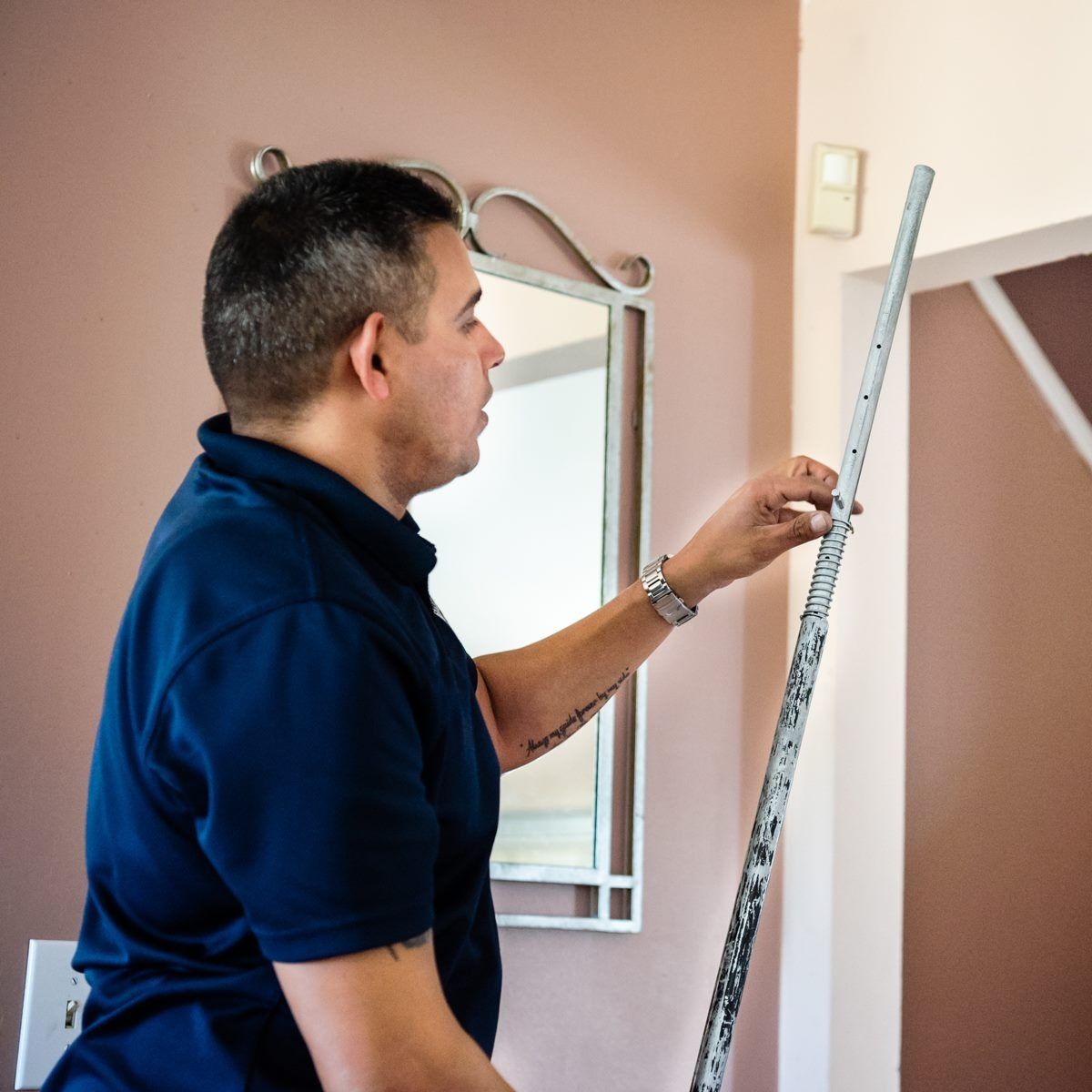 Man in blue shirt measures a wall with a measuring stick, interior shot with mirror.