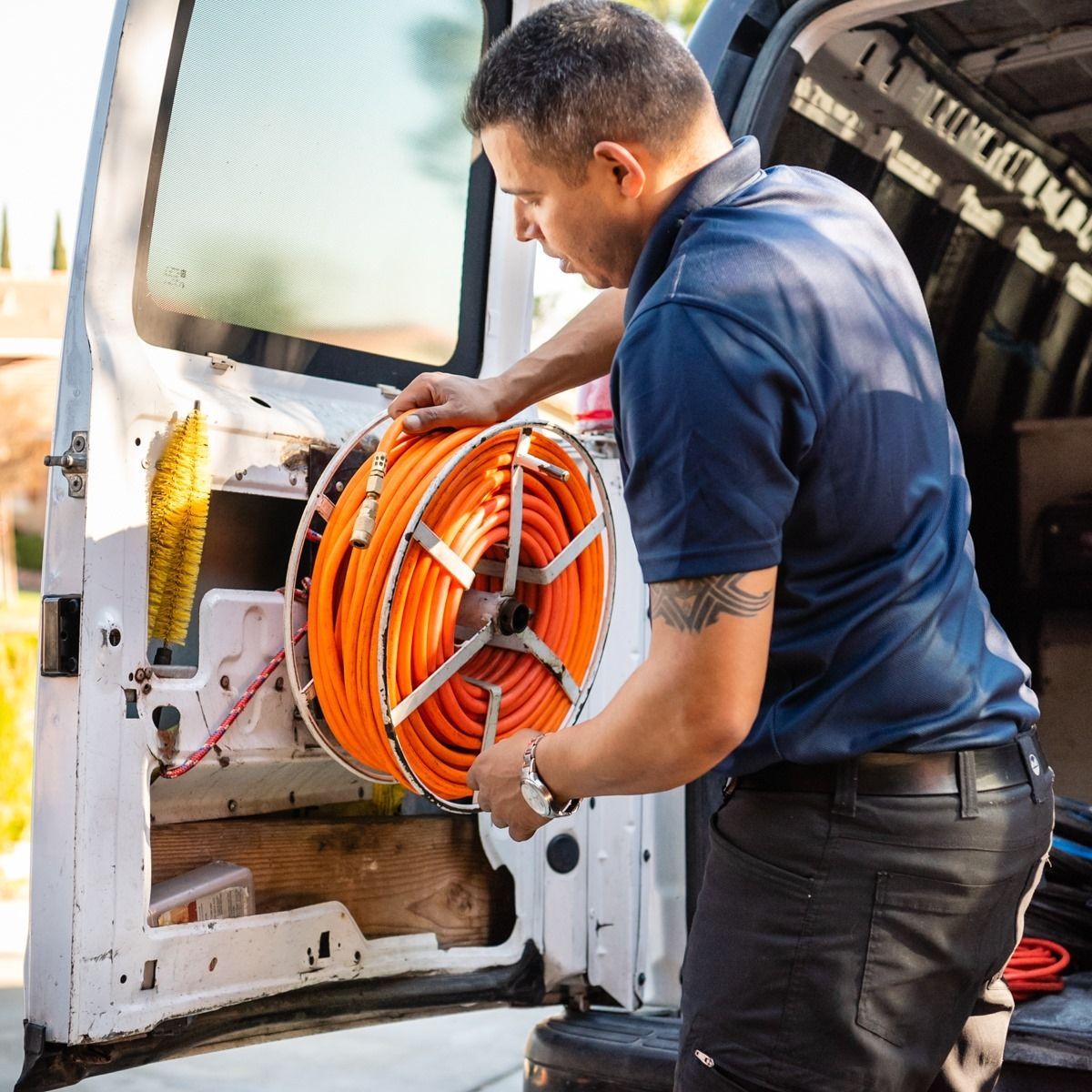 Man in blue shirt loading orange cable spool into a white van.
