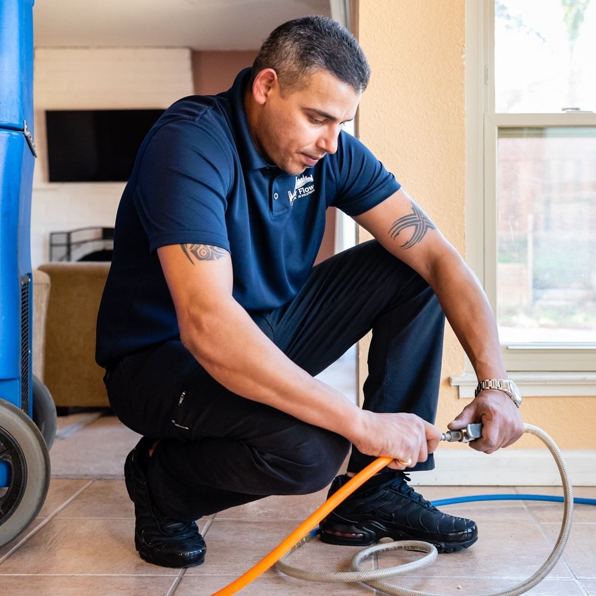 Man in blue shirt and black pants connects a hose indoors, preparing to work.