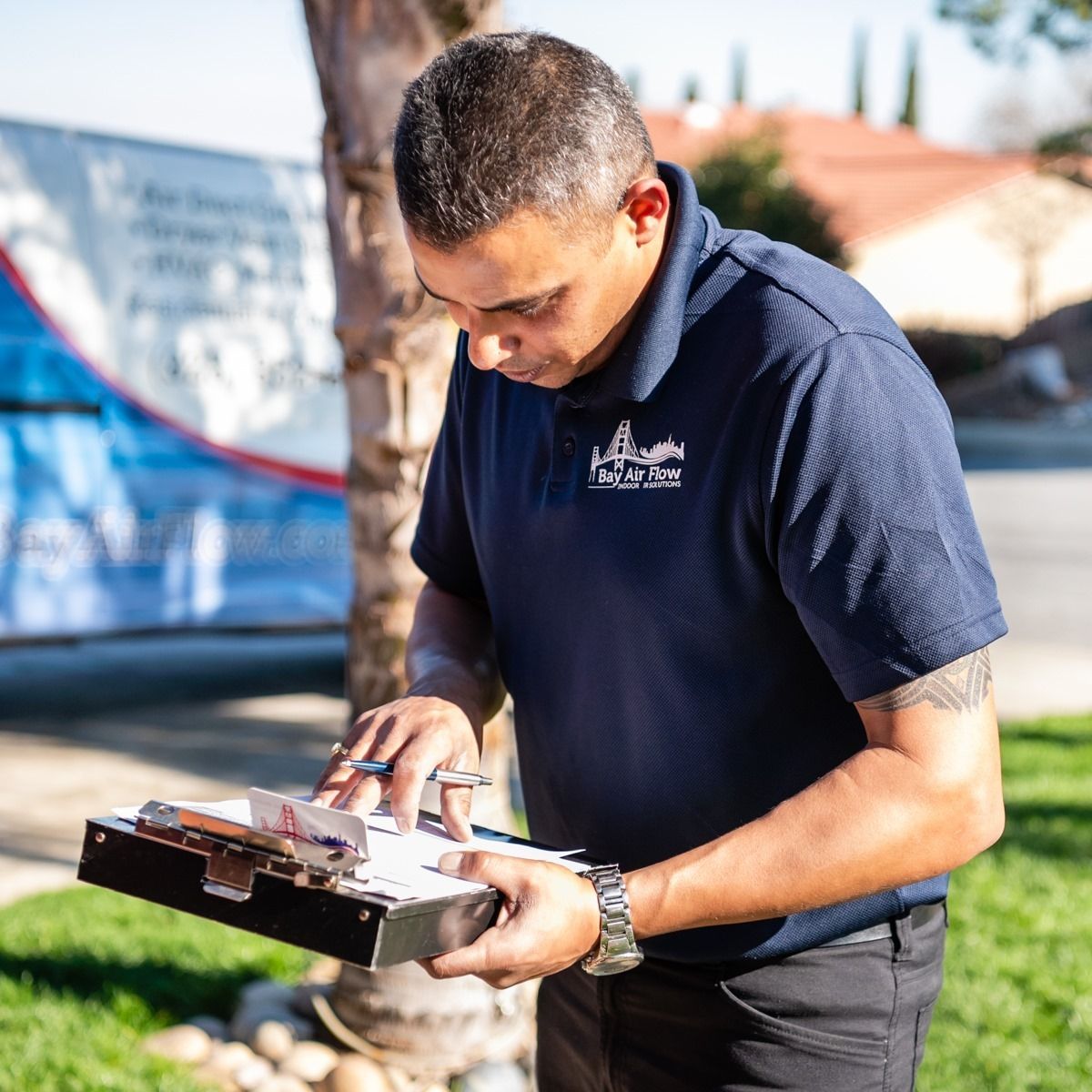 Man in navy polo shirt, inspecting documents on a clipboard outdoors.