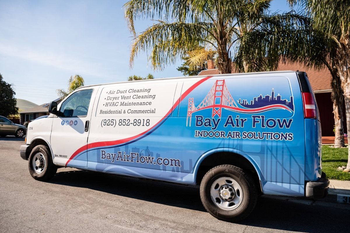 White and blue van parked on a street with Bay Air Flow logo. The van has a design with the Golden Gate Bridge.