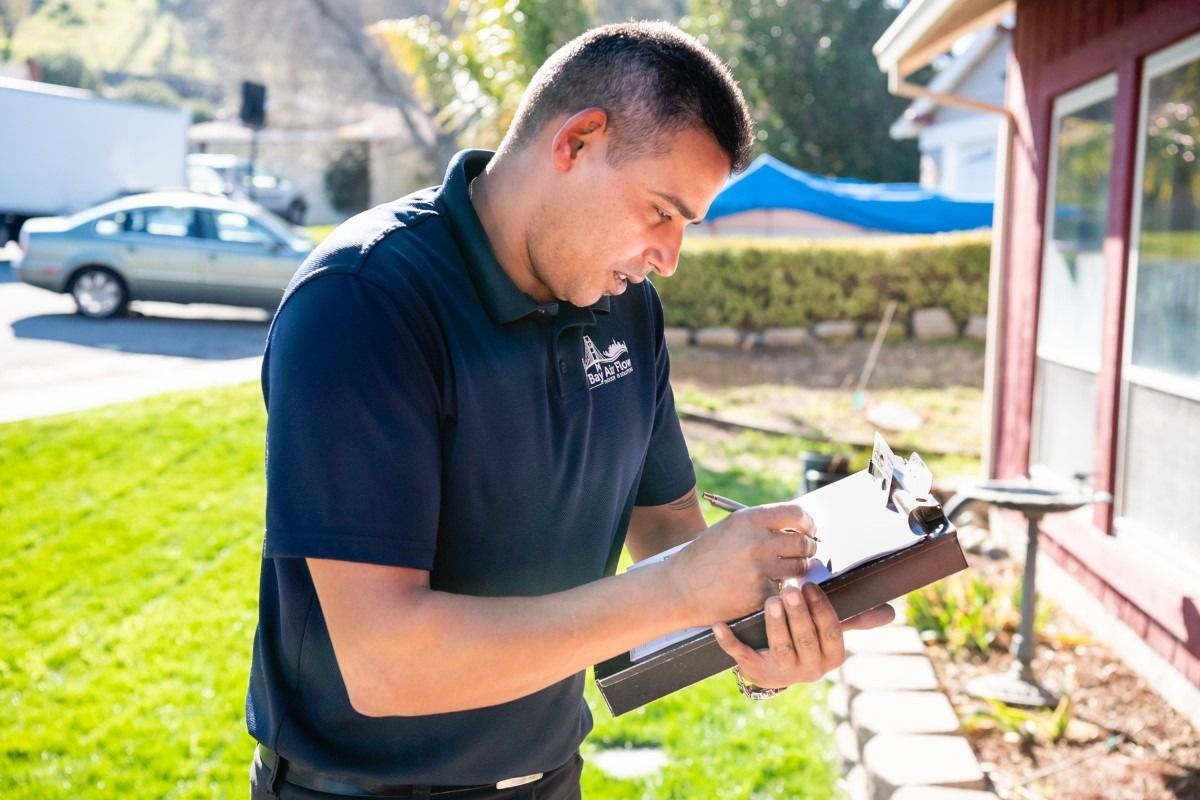 Man in blue shirt outside a house, writing on a clipboard.