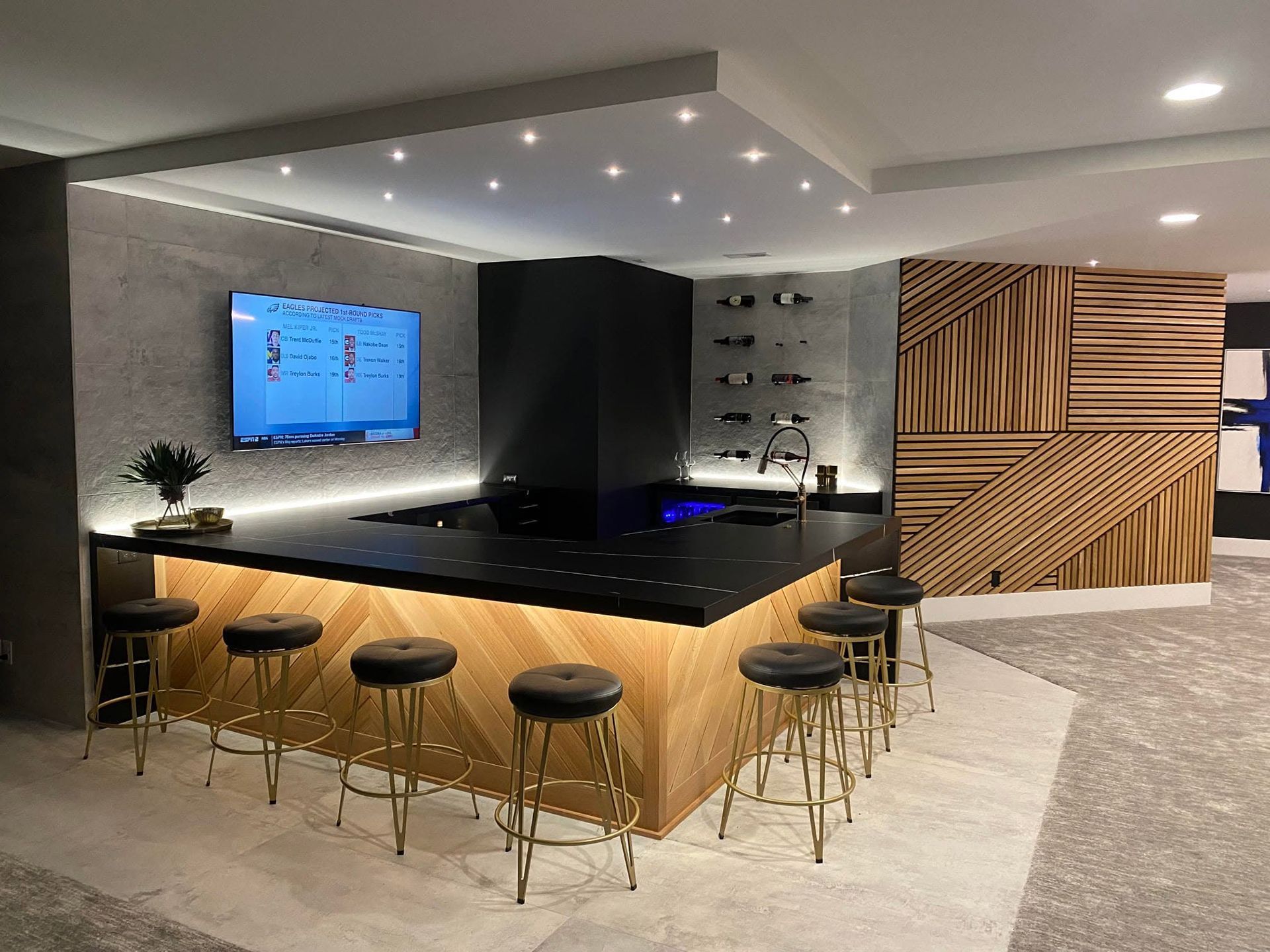 Modern lounge with a black bar, stools, wall TV, and wood accent panels on a carpeted floor