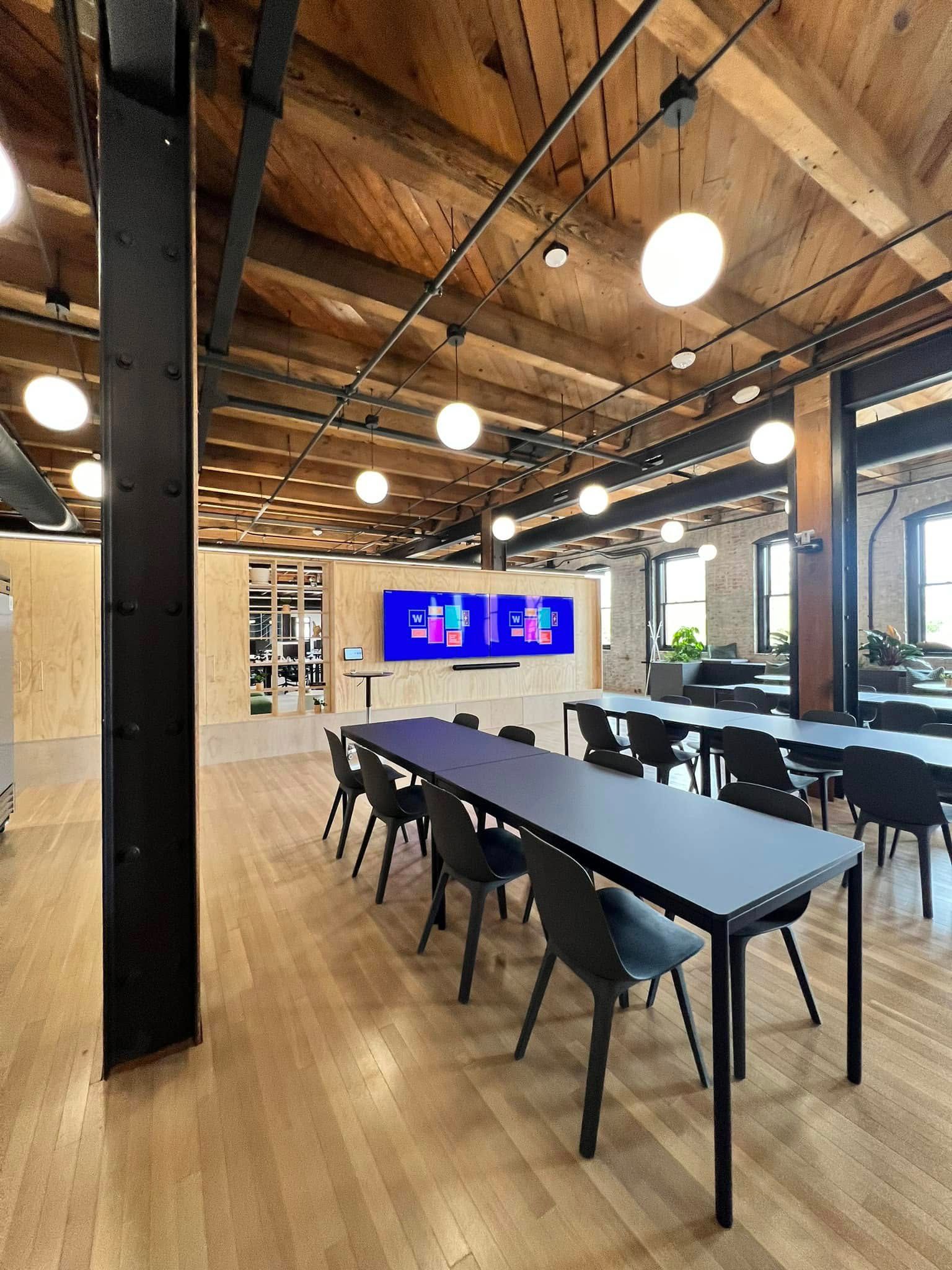 Modern conference room with long black table, chairs, wood ceiling, and wall-mounted display screens.