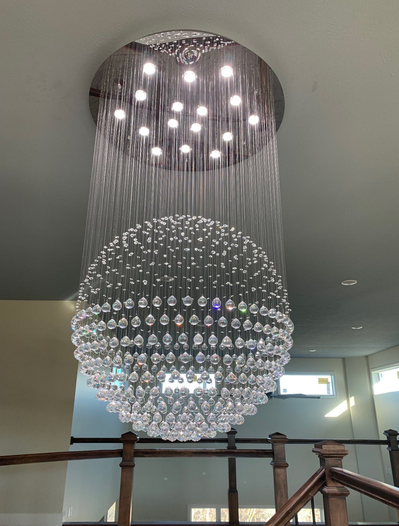 Large crystal chandelier hanging in a lobby stairwell with cascading hanging beads and round lights above.