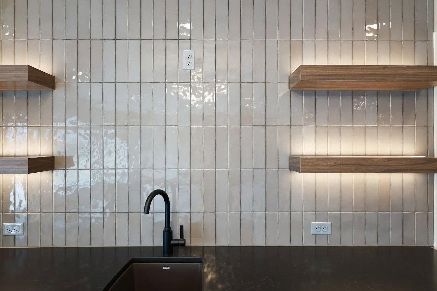 Modern kitchen backsplash with floating wood shelves and a black faucet over a dark countertop