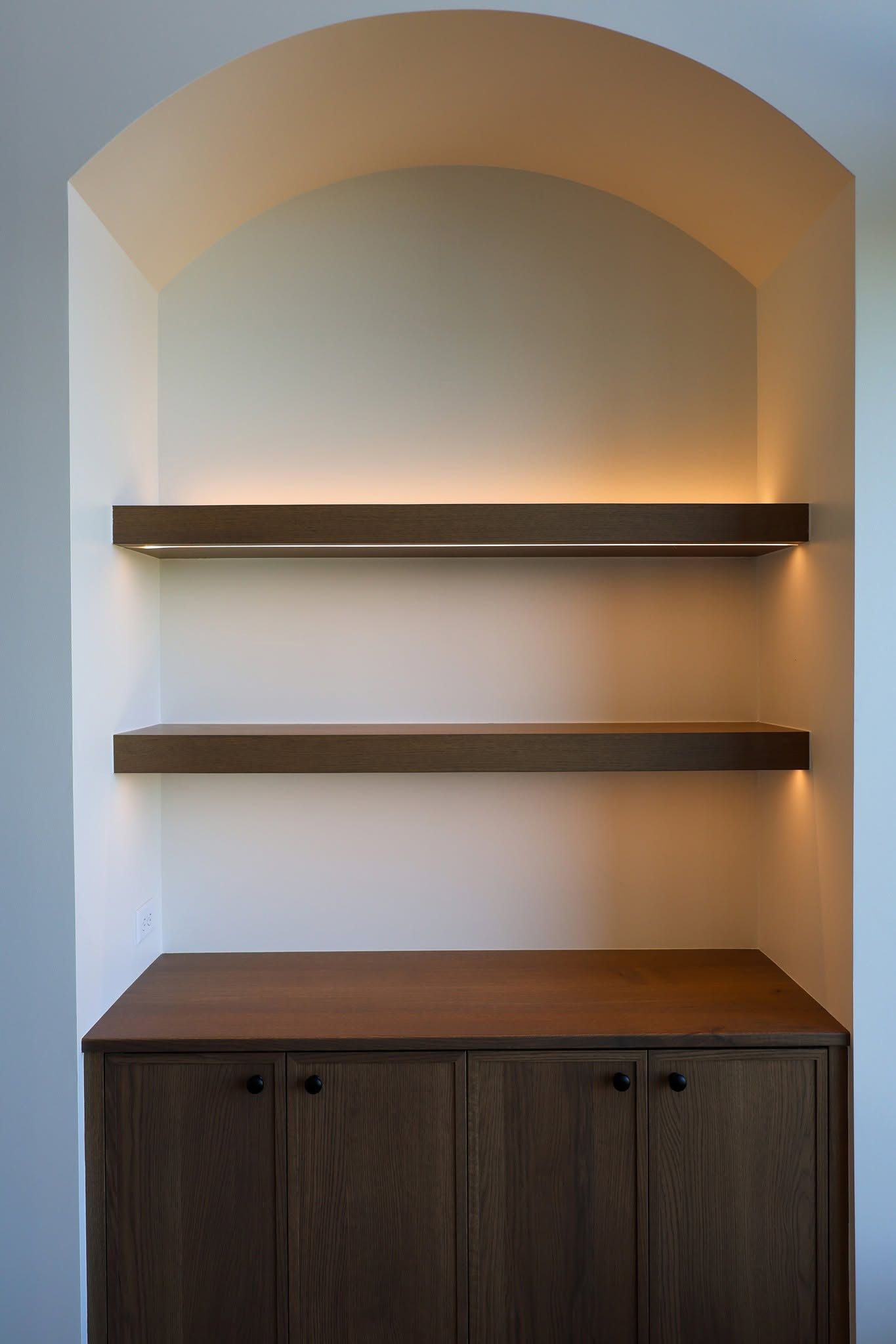 Built-in wall niche with two floating shelves, warm lighting, and a dark wood cabinet below.