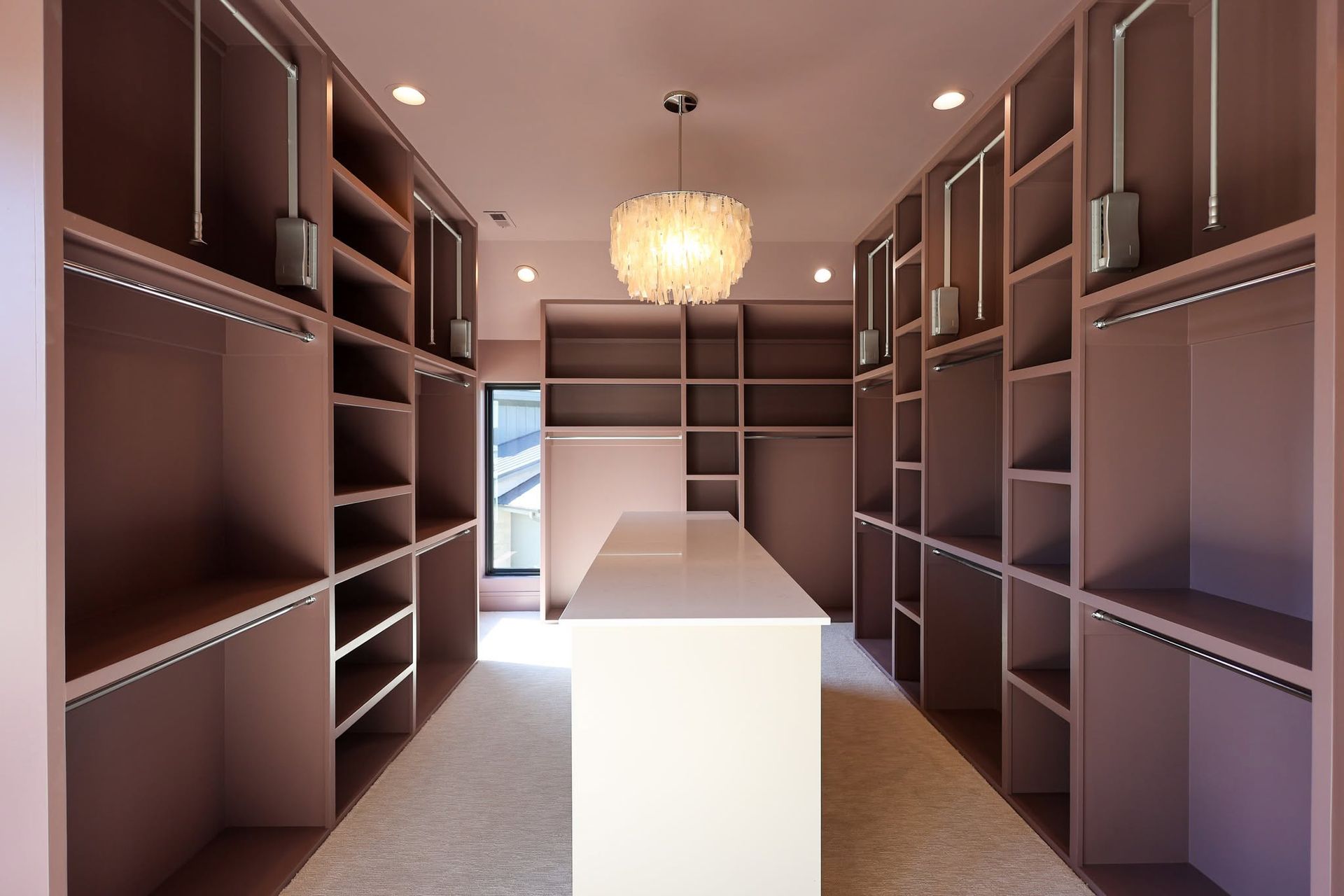 Walk-in closet with brown shelving and a white island under a chandelier.