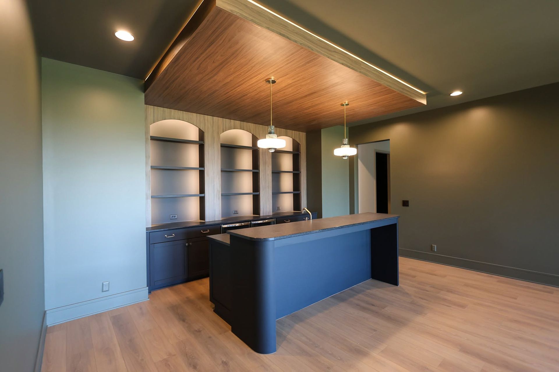 Modern empty kitchen with dark cabinetry, blue island, wood ceiling, and light wood floors