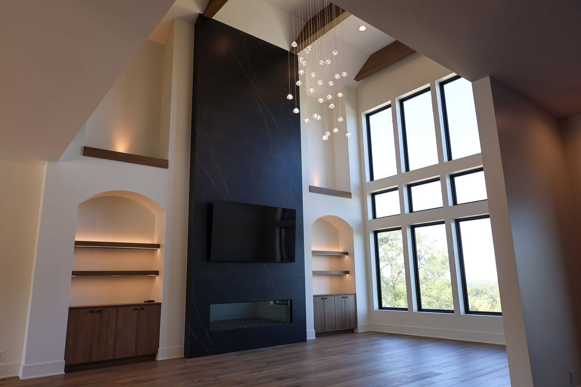 Modern living room with tall windows, dark fireplace wall, arched alcoves, and wood floors