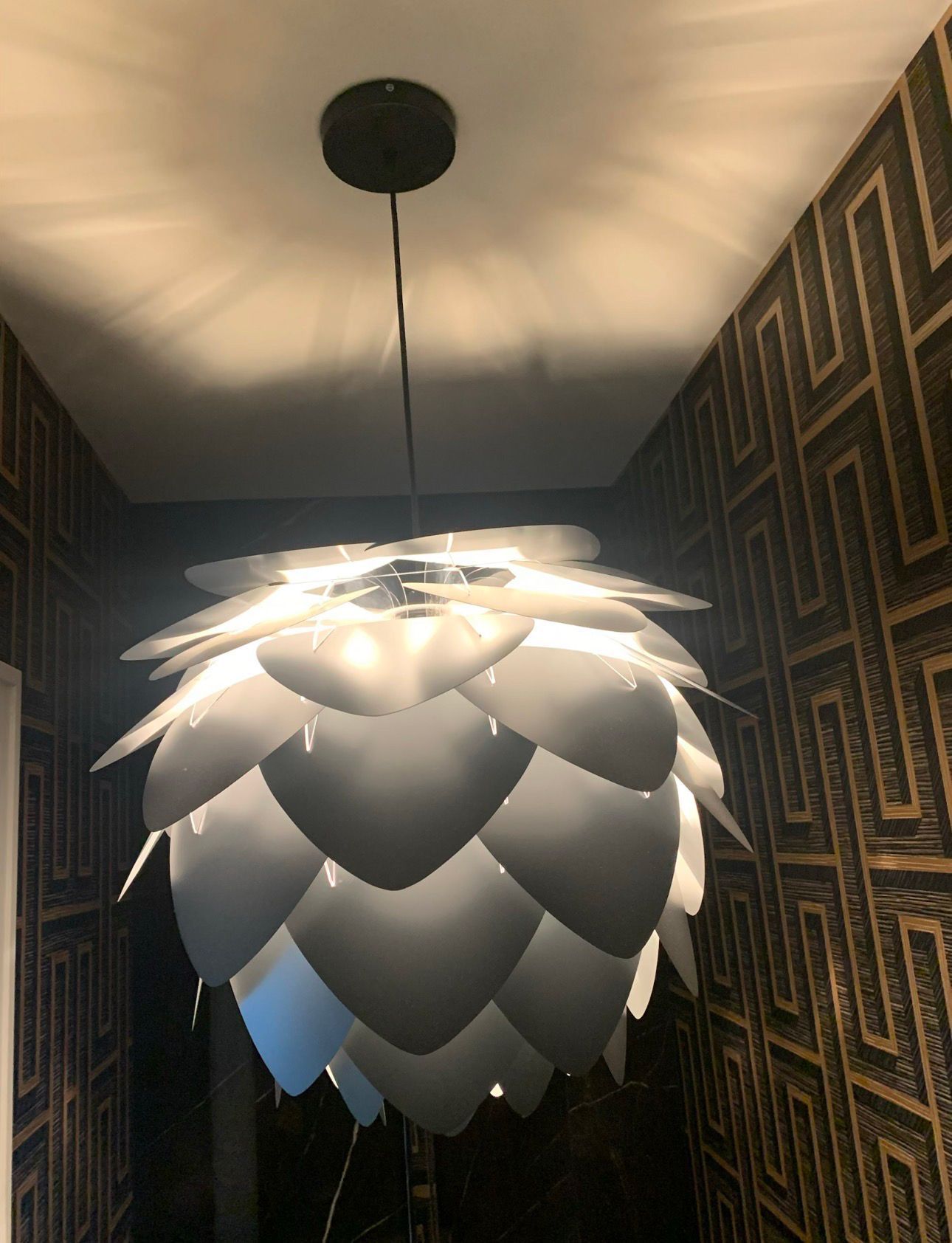 Modern pendant light with layered silver leaves hanging in a patterned hallway