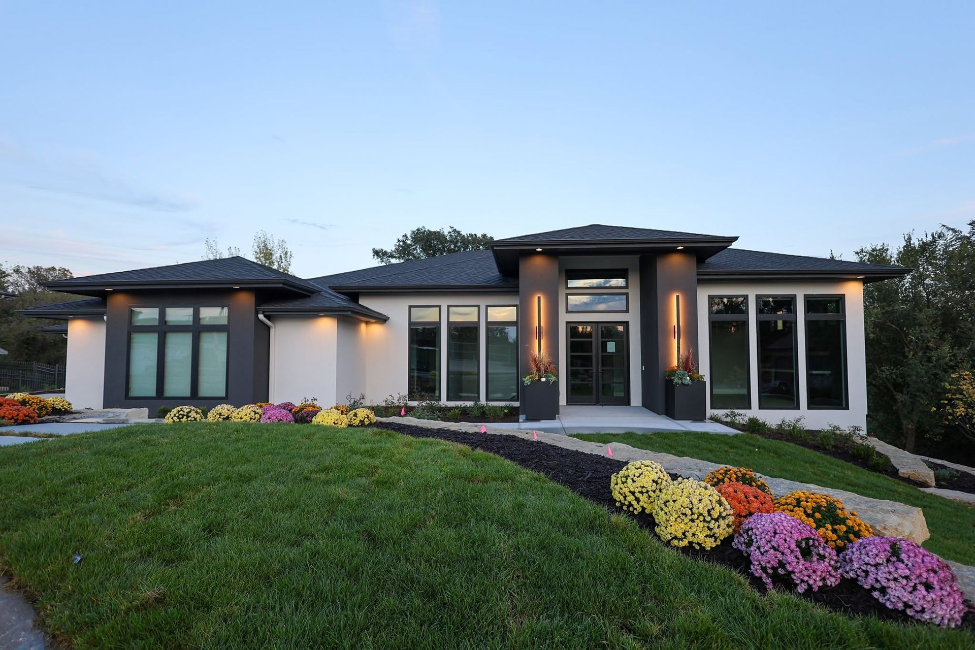 Modern single-story house at dusk with landscaped front lawn and colorful flower beds