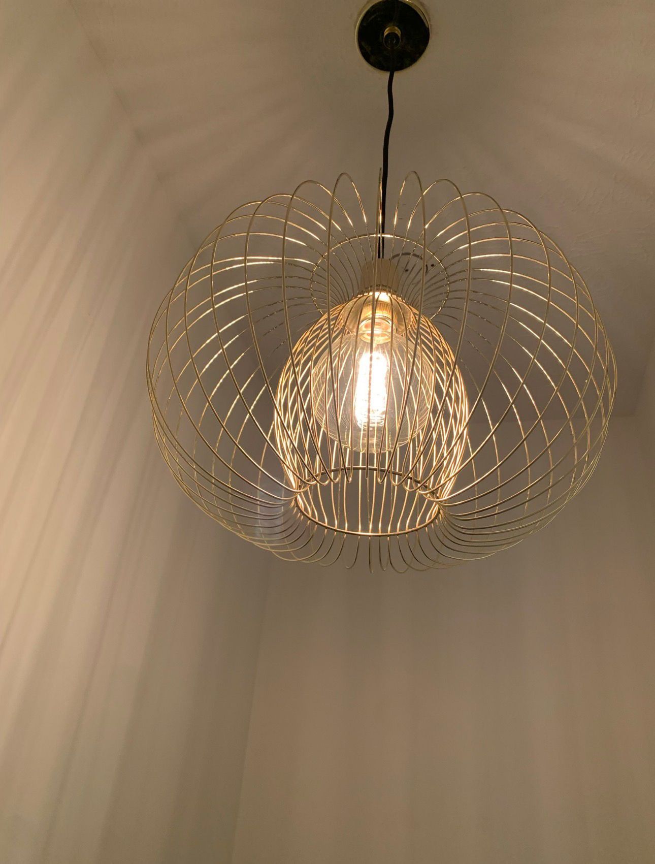 Modern pendant ceiling light with a glowing bulb and intricate gold wire shade in a room corner