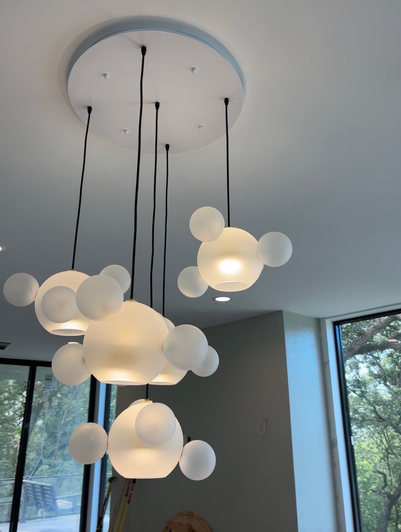 Modern hanging chandelier with white globe lights in a bright room with large windows