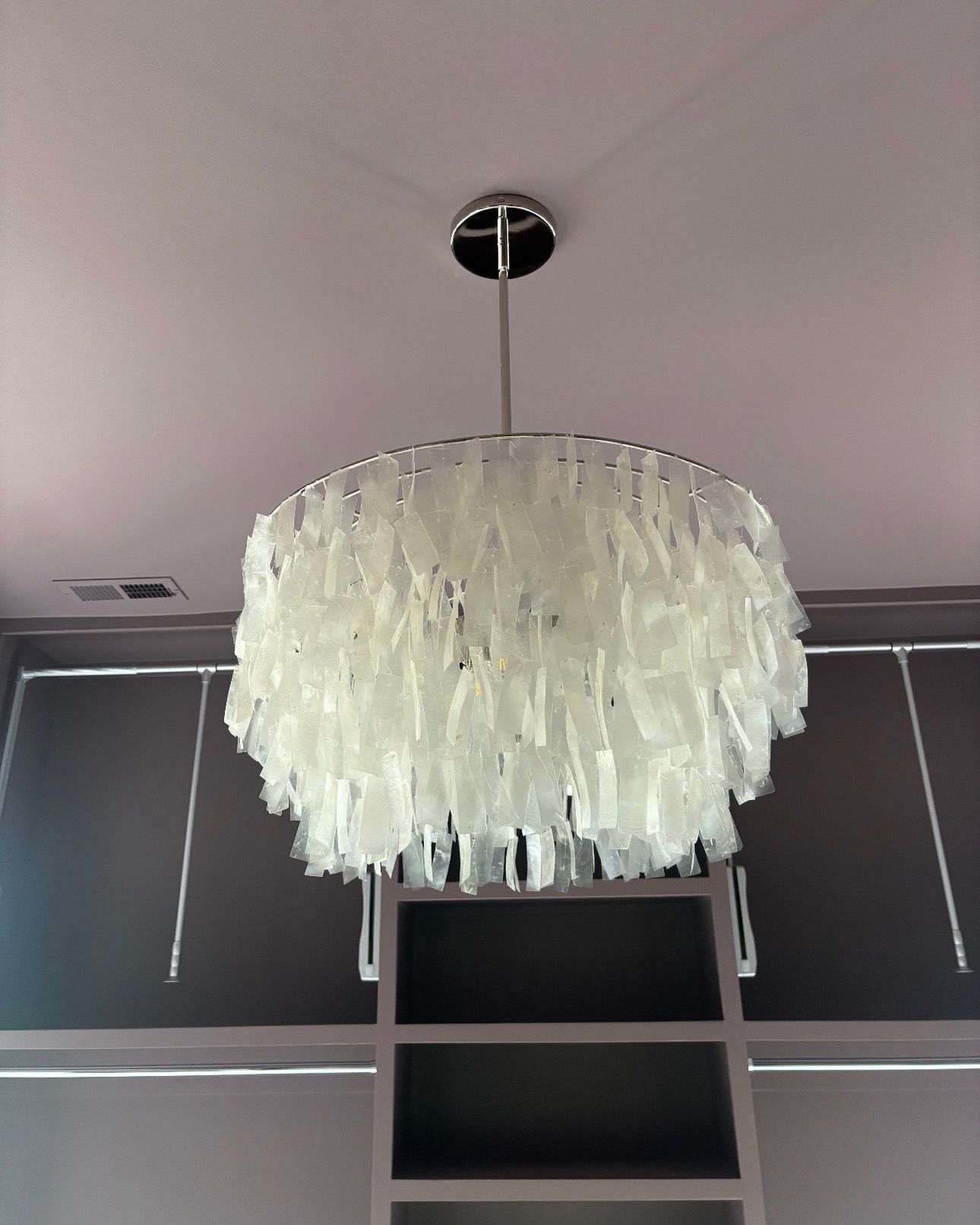 White cascading chandelier hanging from the ceiling above dark window blinds and a ladder
