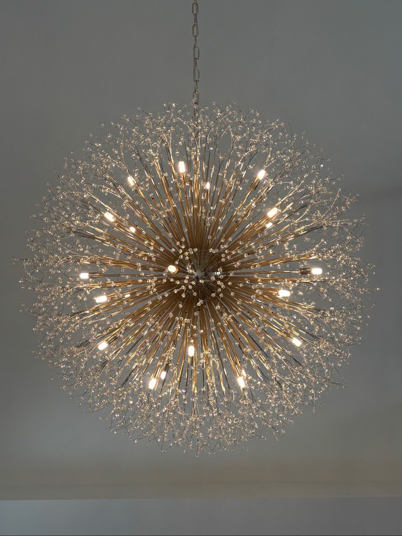 Gold starburst chandelier hanging from a ceiling, glowing with many small lights