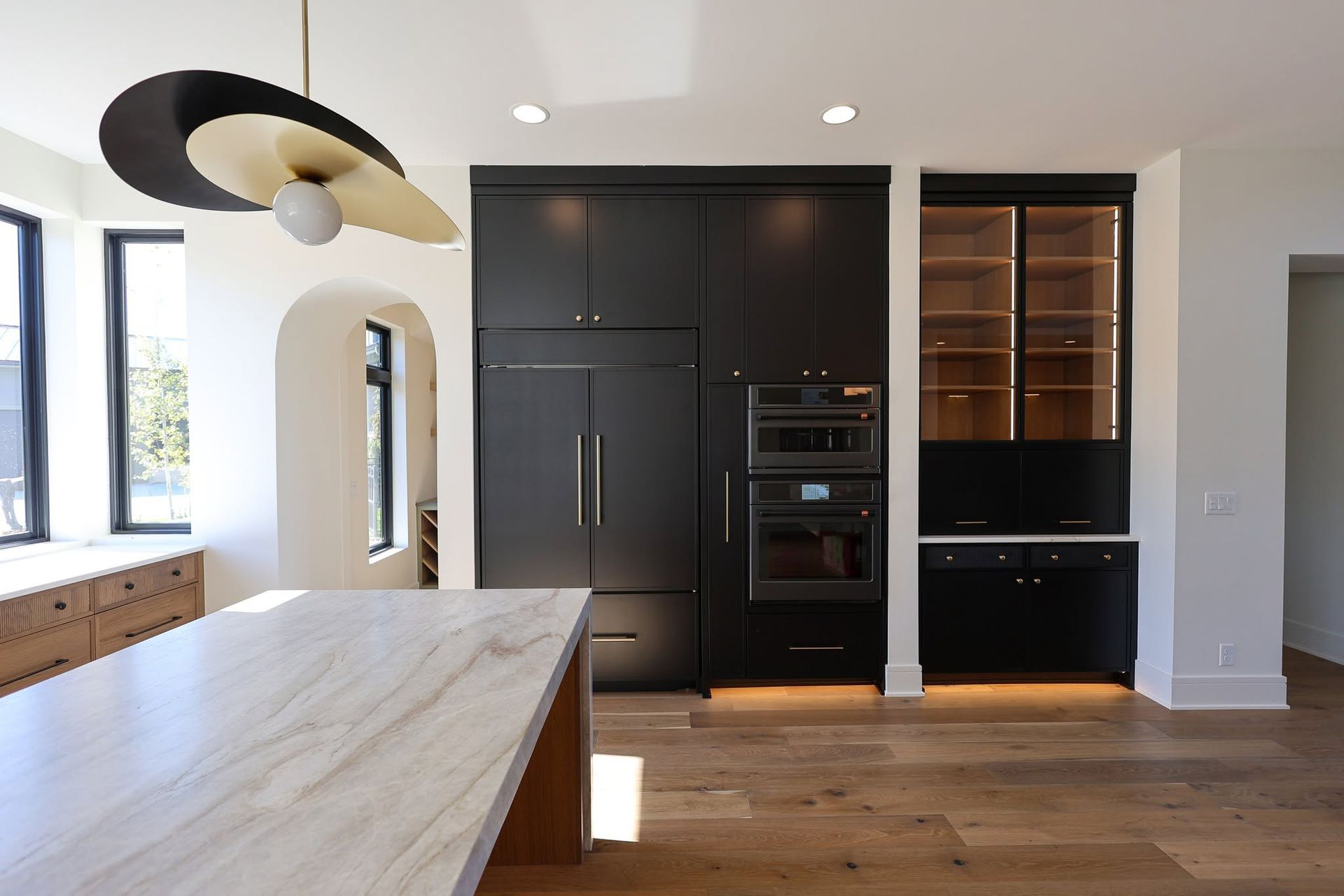 Modern kitchen with black cabinets, built-in ovens, wood floor, and large island near bright windows