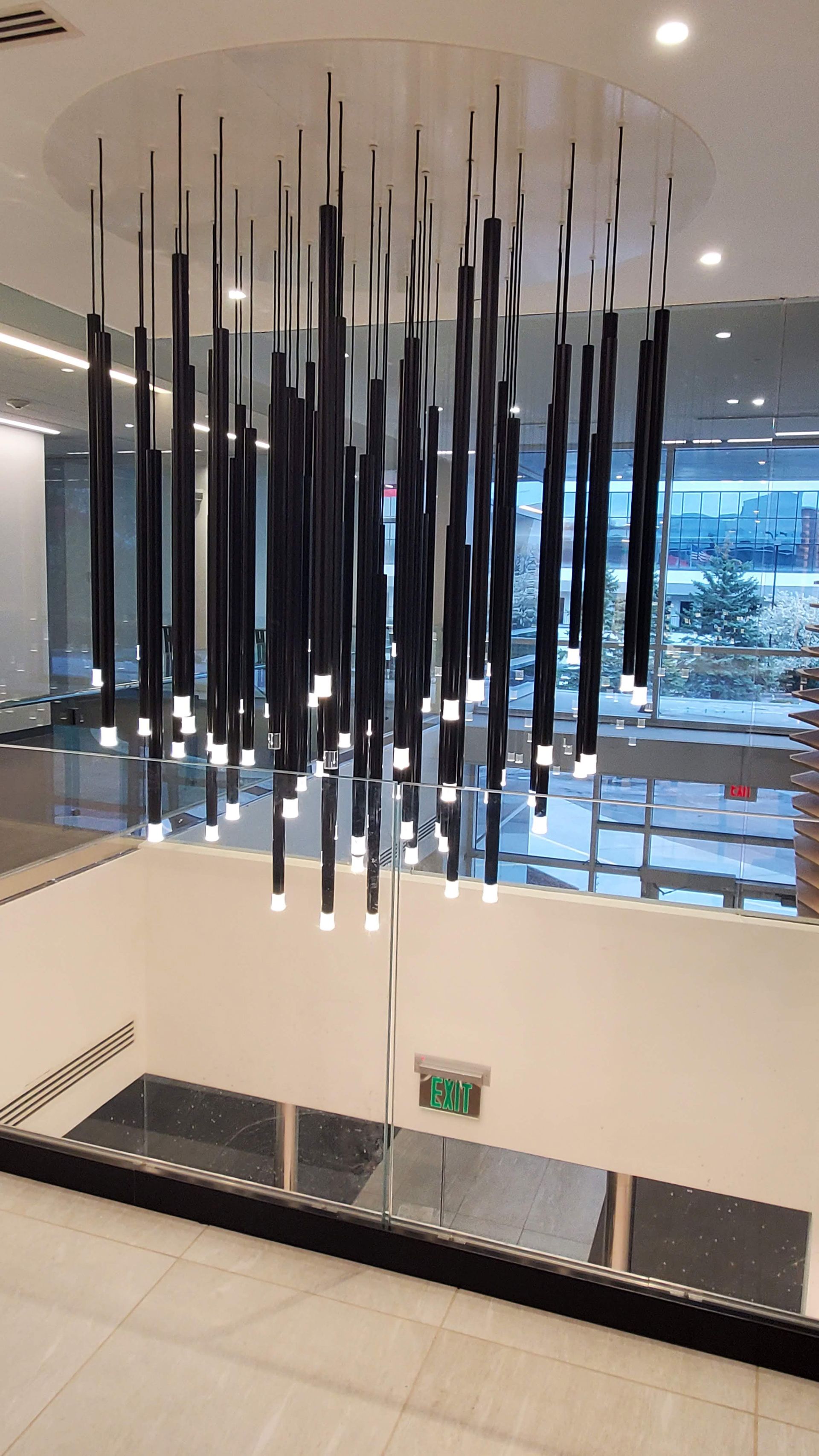 Modern lobby with hanging black sculptural lights over a white staircase and glass railing
