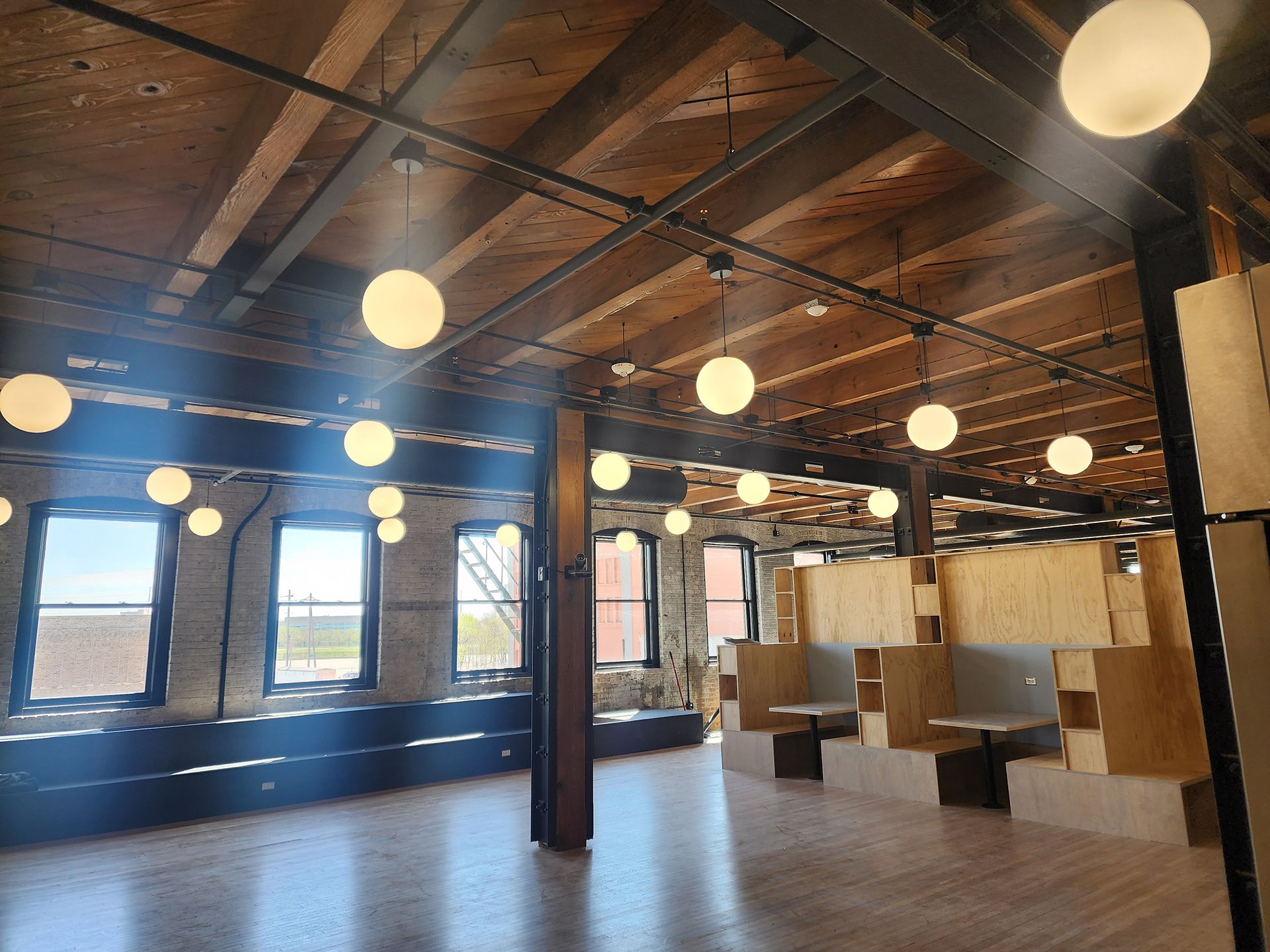 Spacious loft interior with exposed wooden beams, hanging globe lights, and large windows.